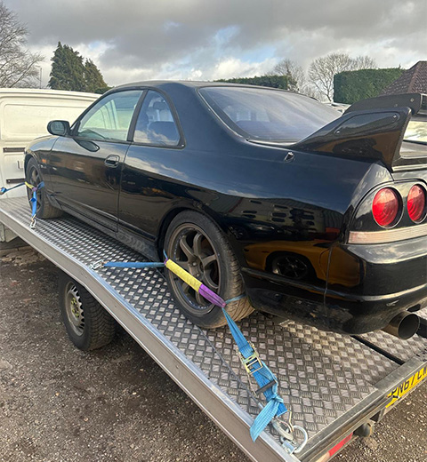 black sports car on trailer secured with straps featuring six cylinder engine and racing wheels