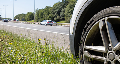 car wheel on grassy verge beside busy highway with vehicles passing by 4 car maintenance tips