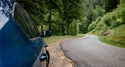 blue car parked on a winding road surrounded by lush green trees and forest scenery perfect for a nature drive or a road trip adventure exploring five scenic routes