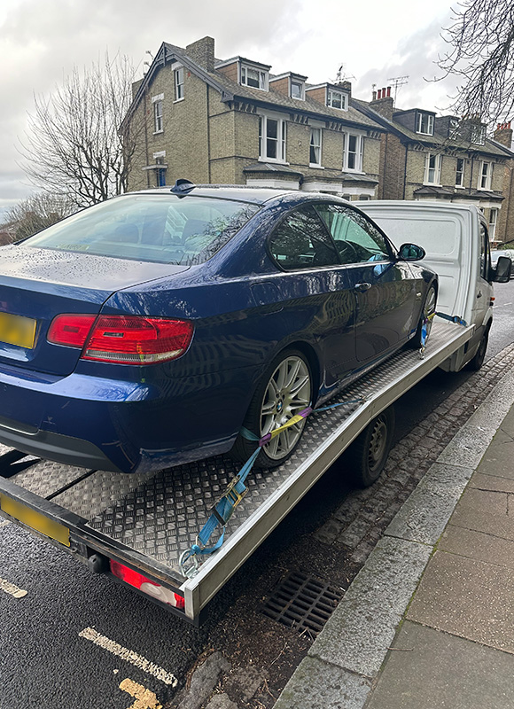 blue car being loaded onto a truck with secured straps parked on a street with residential buildings in the background 8 wheels tow truck services